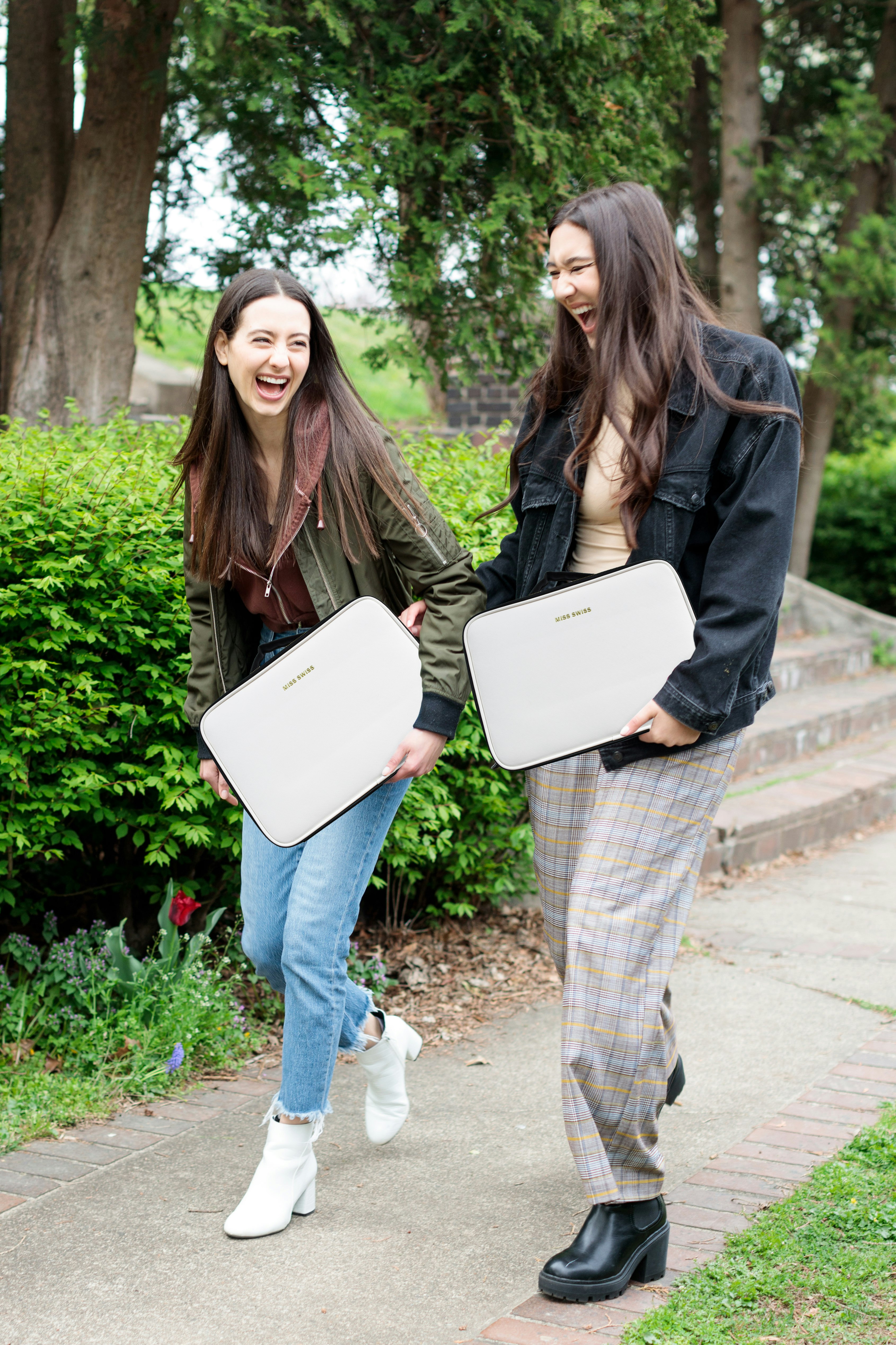 woman in brown jacket and blue denim jeans holding white laptop computer